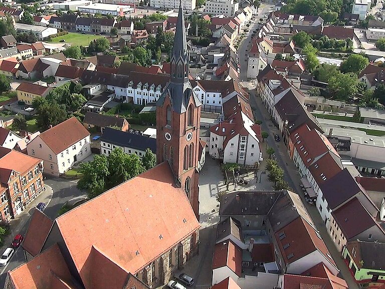 Hier sieht man eine Luftaufnahme von der Innenstadt Gräfenhainichens, im Vordergrund die Evangelische Stadtkirche, links das Paul-Gerhardt-Gymnasium und etwas weiter hinten den Oberen Stadtturm.