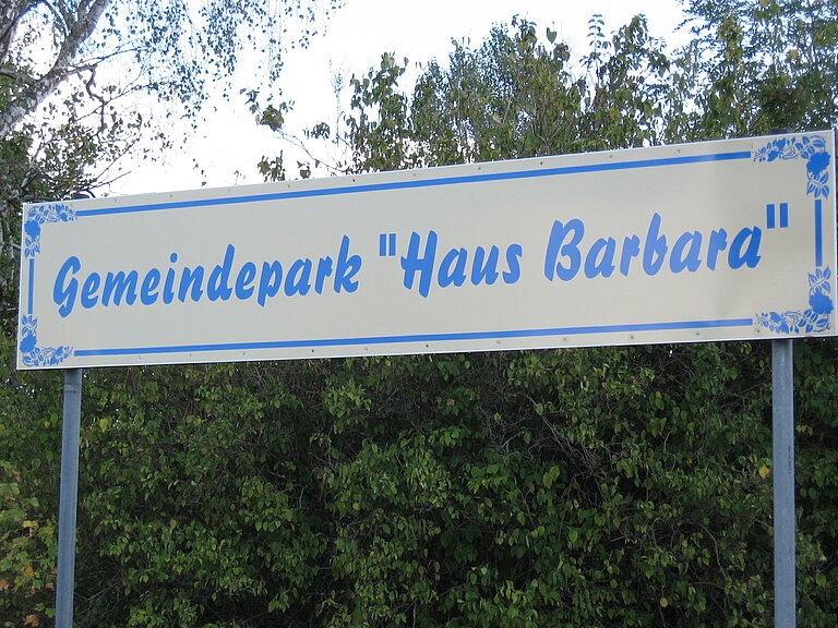Hier sieht man ein Eingangsschild mit der Aufschrift Gemeindepark Haus Barbara.