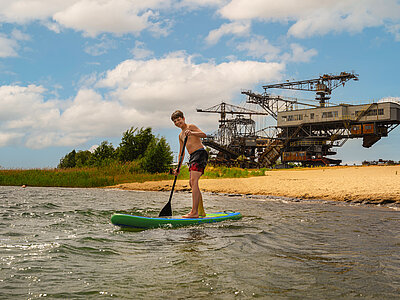 Stand-up-Paddler auf dem Gremminer See. Im Hintergrund sind die Tagebraugroßgeräte von Ferropolis zu sehen.