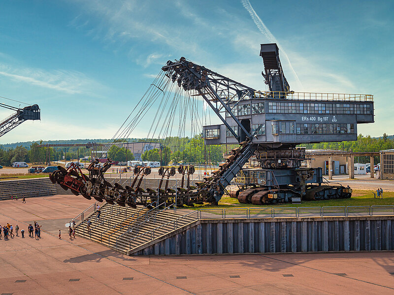 Führung auf dem Gelände der Ferropolis GmbH. Die Gruppe steht vor einem Tagebaugroßgerät.