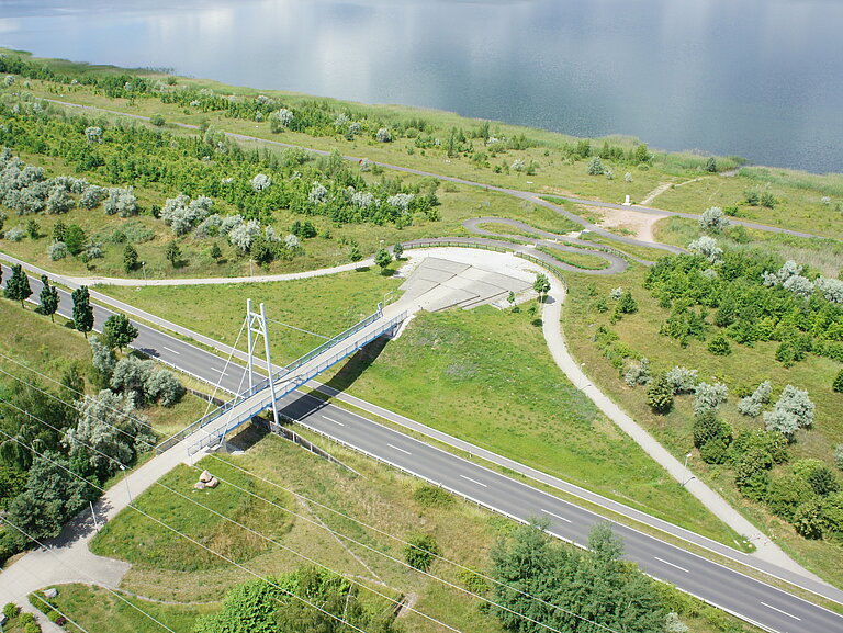 Luftaufnahme der Gremminer Brücke mit Stadtbalkon. Eine kleine Serpentine führt zum Gremminer See.