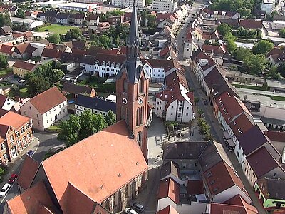 Hier sieht man eine Luftaufnahme von der Innenstadt Gräfenhainichens, im Vordergrund die Evangelische Stadtkirche, links das Paul-Gerhardt-Gymnasium und etwas weiter hinten den Oberen Stadtturm.