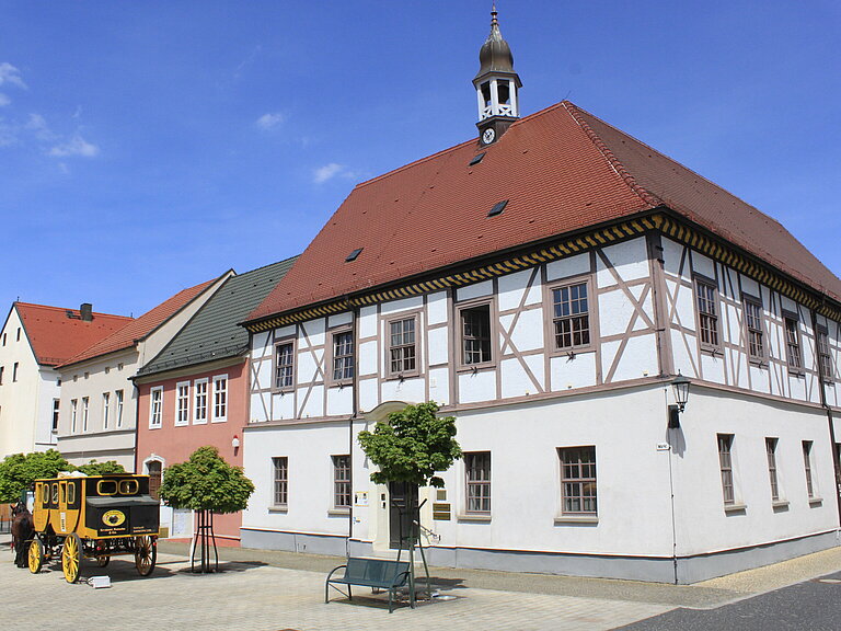Rathausgebäude mit Haupteingang, davor steht gerade eine alte Postkutsche