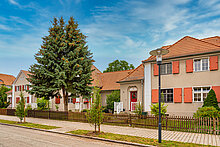 Eine Straße und ein Fußweg bei schönem Wetter. Im Hintergrund stehen Mehrfamilienhäuser.