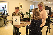 Auf diesem Bild sieht man zwei Besucherinnen die gerade die Preforiermaschine im Buchdruckmuseum Gräfenhainichen erklärt bekommen.
