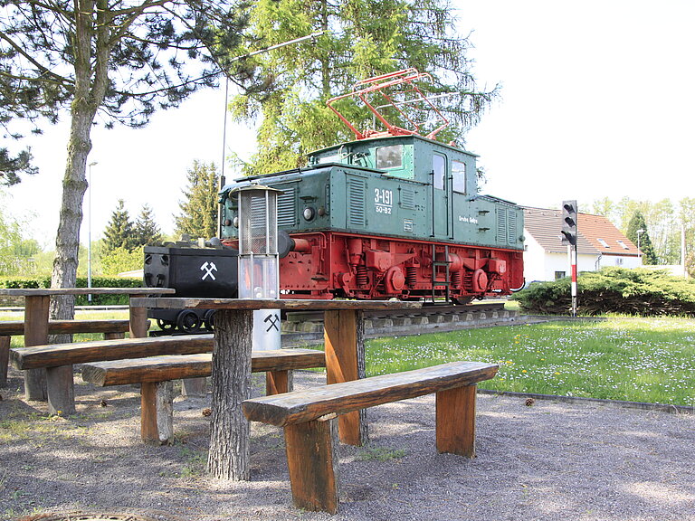 Eine Lok als Bergarbeiterdenkmal in Möhlau, mit Sitzgelegenheiten vor dem Denkmal.