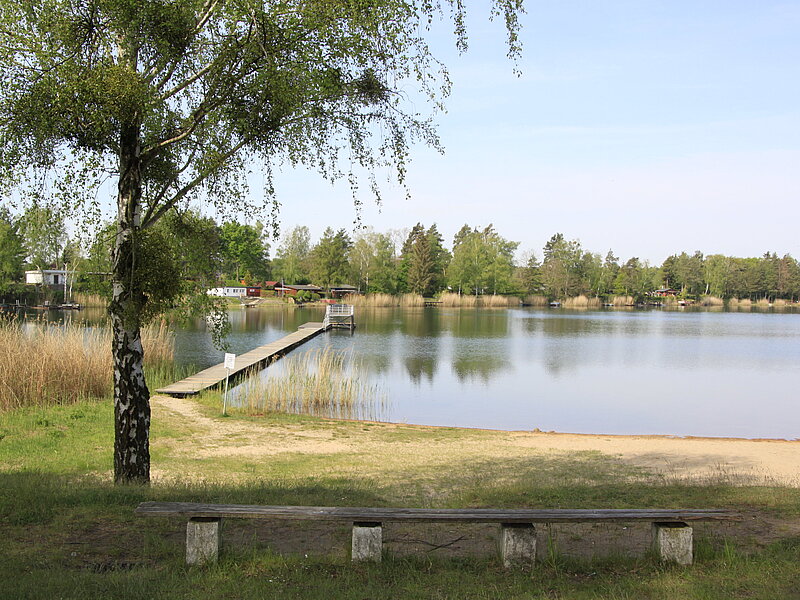 Möhlauer Bad - Blick auf See mit Steg im Hintergrund, Sitzgelegenheiten im Vordergrund.