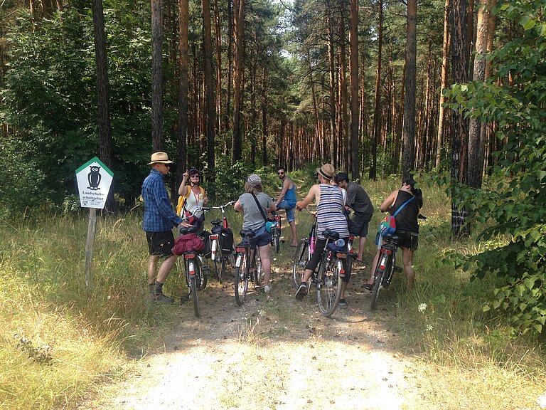 Eine Gruppe Fahrradfahrer hält im Wald und bekommt Wissenswerte zur Natur erläutet.