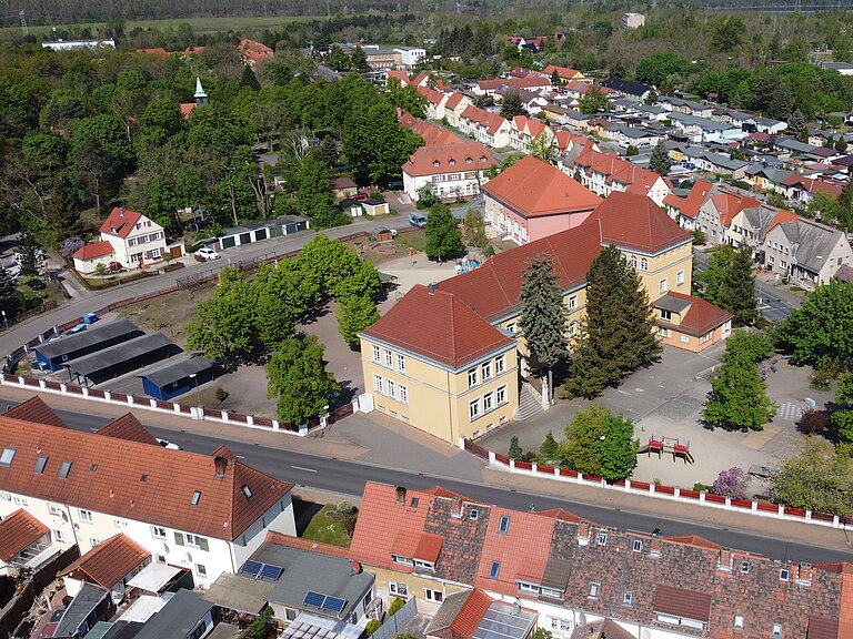 Luftaufnahme der Grundschule und angrenzendem Hort inklusive Pausenhof..