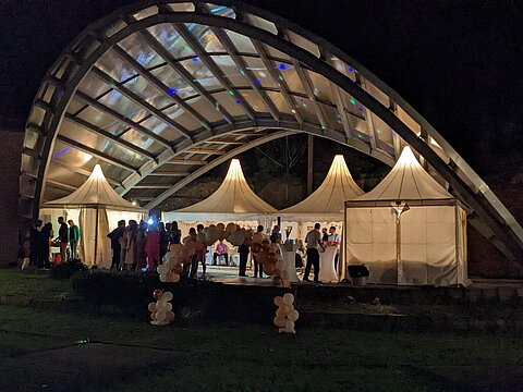 Hier wurde die Freilichtbühne für eine Hochzeit gemietet. Mehrere beleuchtete Pavillons am Abend mit vielen Gästen auf der Bühne.