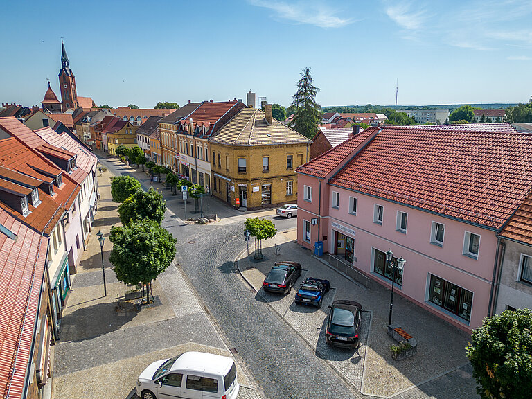 Tourist-Info aus der Lustperspektive. Parkbuchten mit parkenden Autos davor. Blick Richtung Kirche und Boulevard.