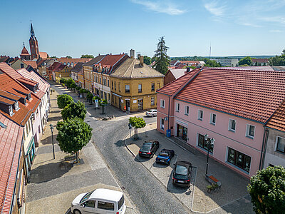 Tourist-Info aus der Lustperspektive. Parkbuchten mit parkenden Autos davor. Blick Richtung Kirche und Boulevard.