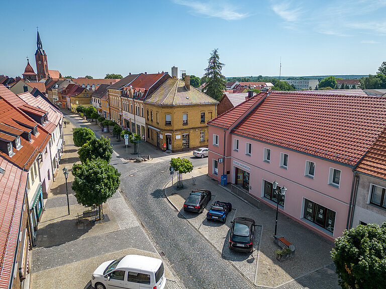 Tourist-Info aus der Lustperspektive. Parkbuchten mit parkenden Autos davor. Blick Richtung Kirche und Boulevard.